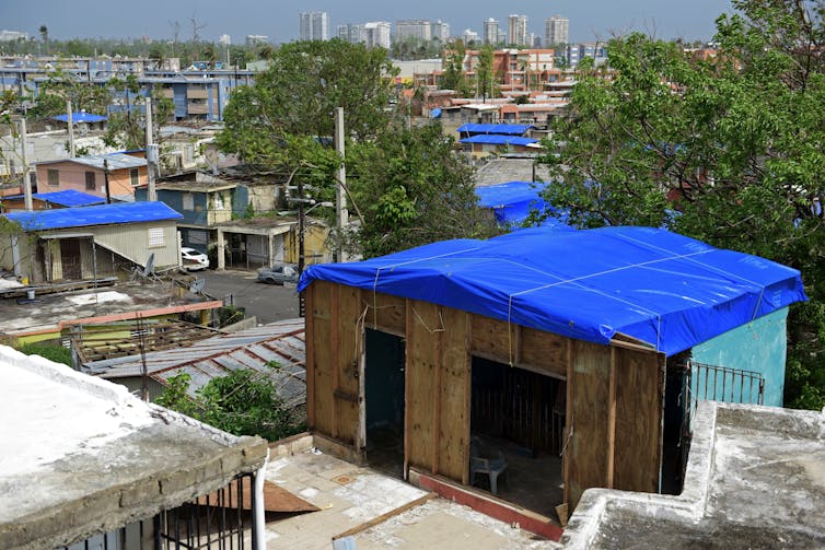 Houses in a sunny place with their roofs blown off and replaced temporarily by tarps.