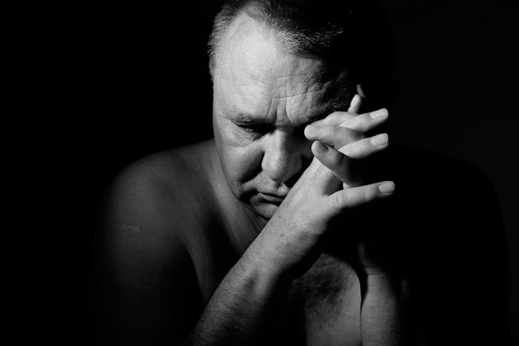 A sad older man with eyes closed and hands clasped