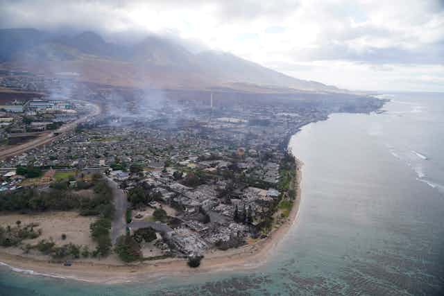 An aerial view showing smoke rising around mountains and burnt homes.