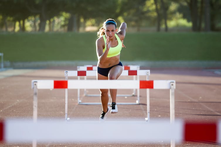 Woman jumping over a hurdle during training on race track