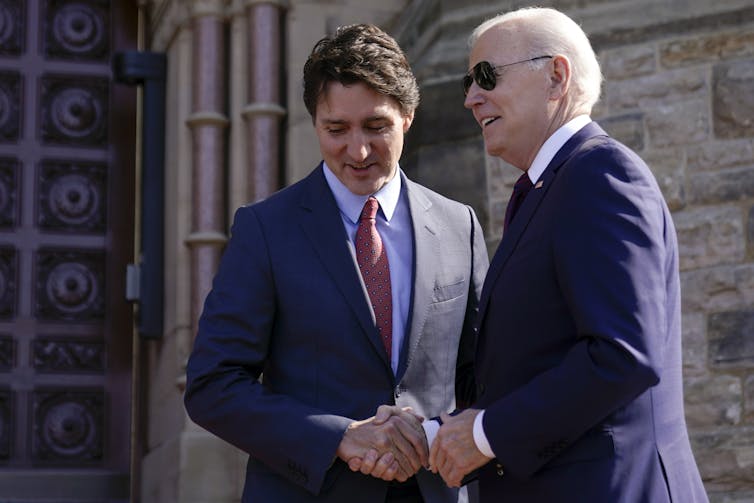 Trudeau and Biden shake hands at the entrance to a stone building.