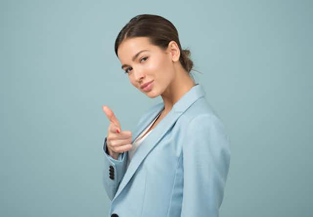 A woman in a light blue blazer giving a thumbs up sign
