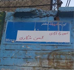 Part of an official street sign is painted over with handwriting.