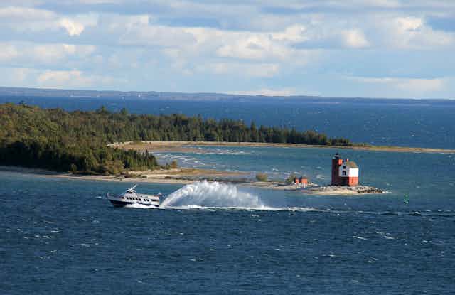 A ferry passes the end of a wooded island and a lighthouse