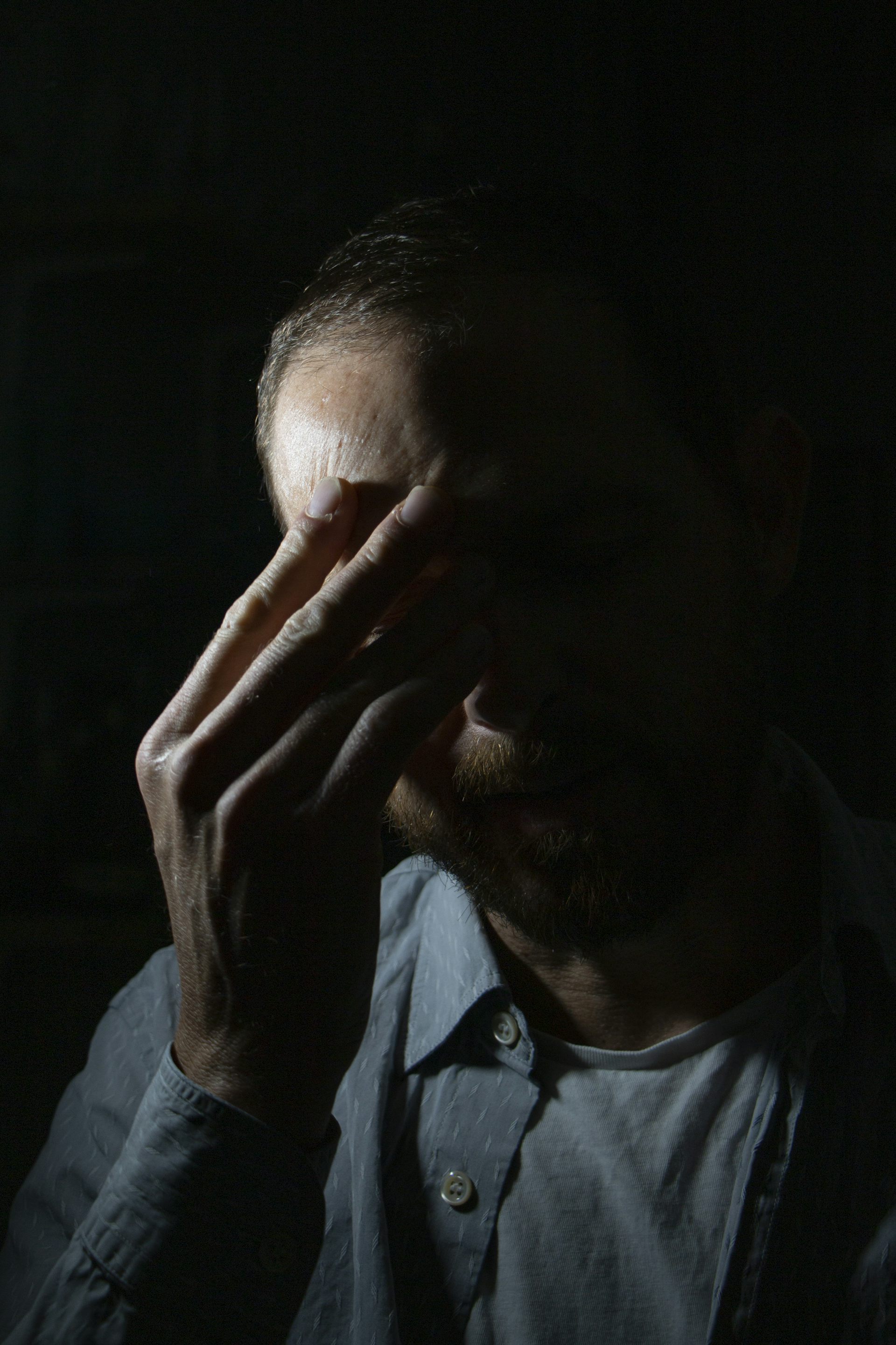 Emotional portrait photograph of a scientist experiencing 'climate emotions', showing the face of a man covering his face with his hands, against a black background.