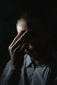 Emotional portrait photograph of a scientist experiencing 'climate emotions', showing the face of a man covering his face with his hands, against a black background.