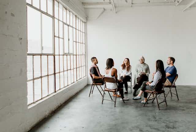 A diverse group of six people sitting on chairs and facing each other in a supportive circle