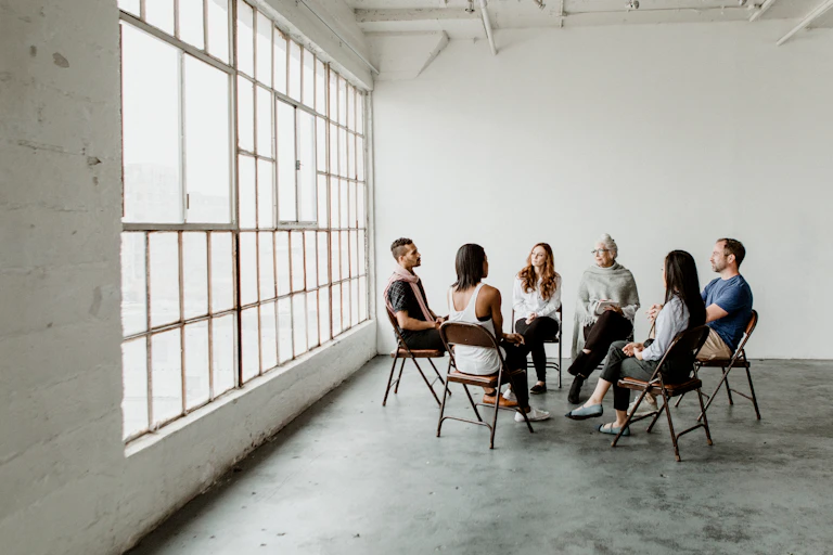 A diverse group of six people sitting on chairs and facing each other in a supportive circle