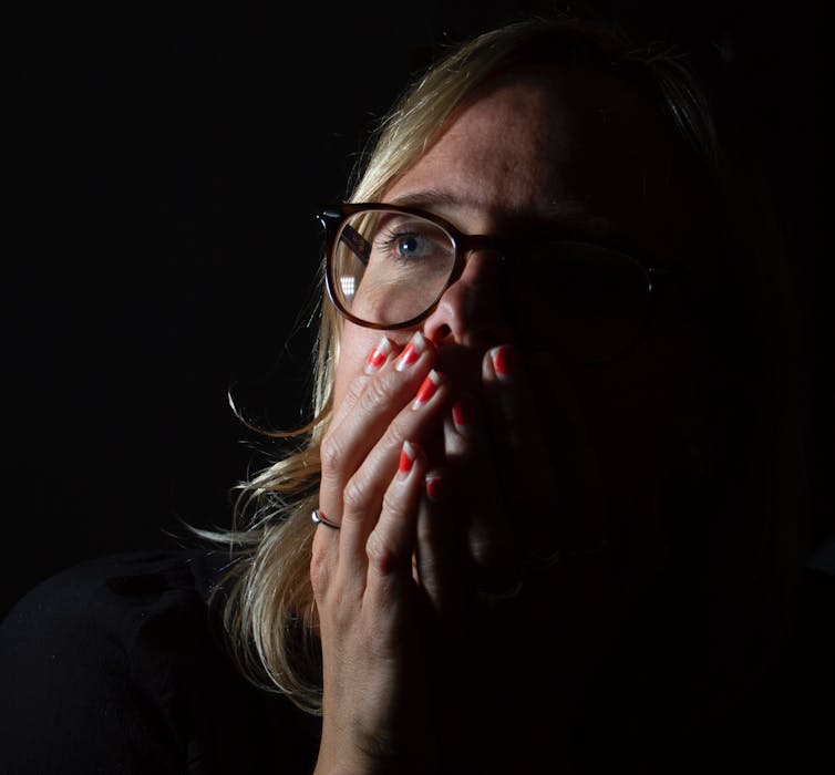 Emotional portrait photograph of a scientist experiencing 'climate emotions', showing the face of a woman looking up and covering he mouth against a black background.