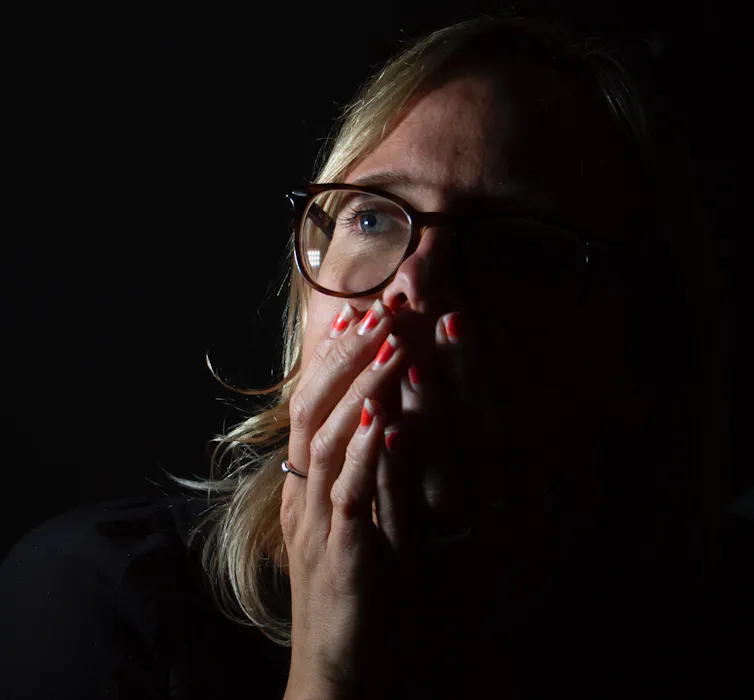 Emotional portrait photograph of a scientist experiencing 'climate emotions', showing the face of a woman looking up and covering he mouth against a black background.