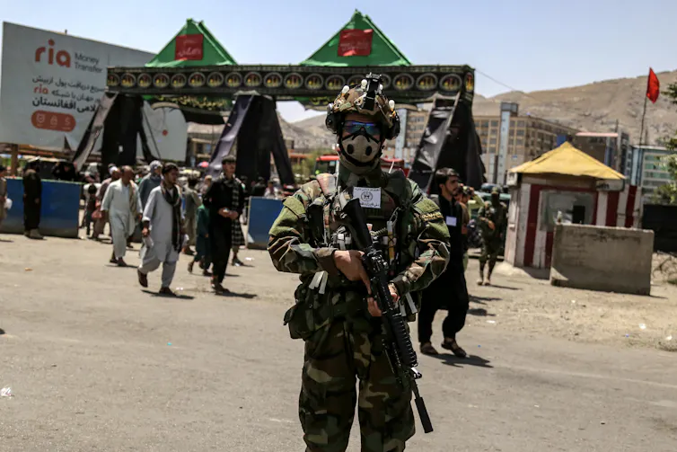 An armed Taliban soldier stands in fromt of a small procession of citizens to mark a local festival.