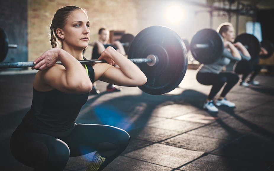 A woman squats with a barbell across the front of her shoulders. 