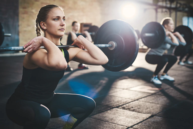 A woman squats with a barbell across the front of her shoulders.