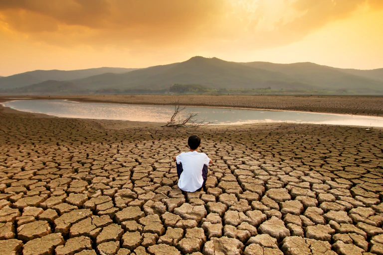 A child sat on a drying lake.