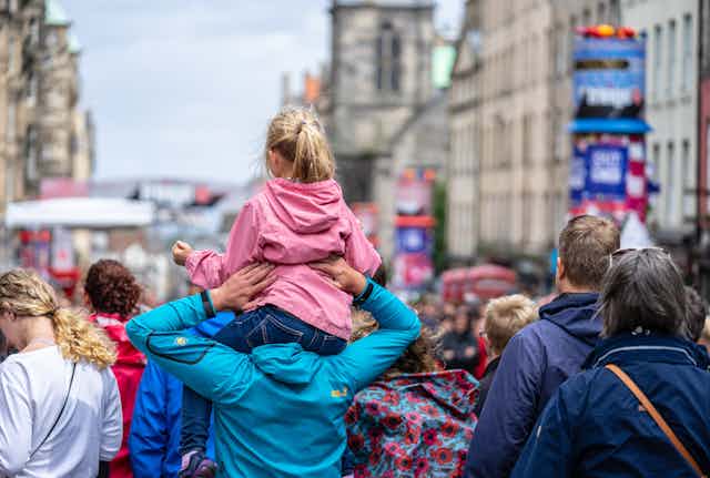 A girl on her dad's shoulders at Edinburgh Fringe in a busy street