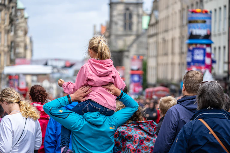 A girl on her dad's shoulders at Edinburgh Fringe in a busy street