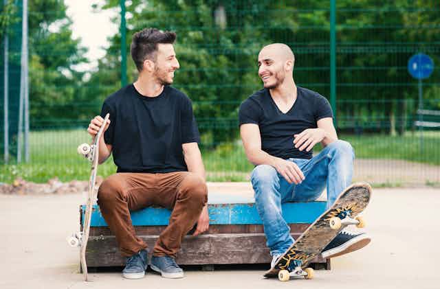Two men with skateboards sit talking