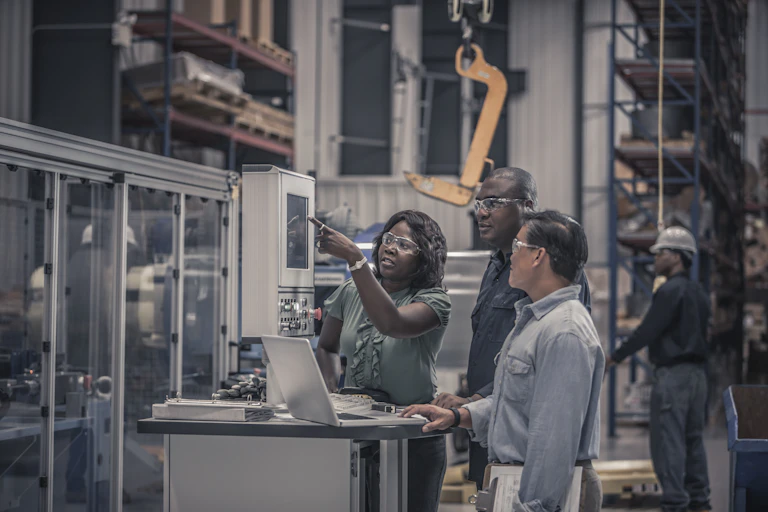 A group of engineers point at a piece of machinery on a factory floor.