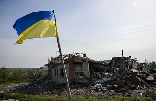 A blue and yellow flag is raised above a destroyed building.