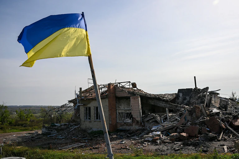 A blue and yellow flag is raised above a destroyed building.