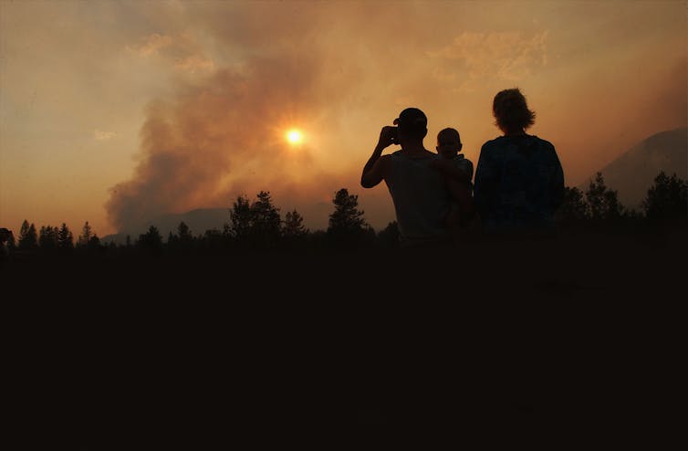 A silhouetted family watches as smoke rises from the Robert Fire in Glacier National Park, near West Glacier, Montana