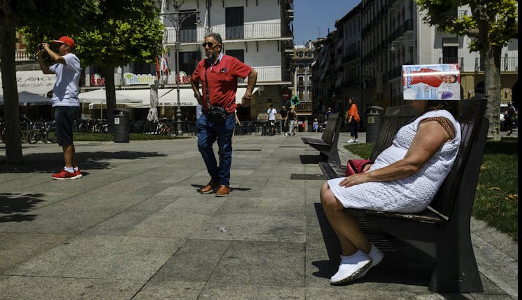 women sits with magazine on head as others walk past