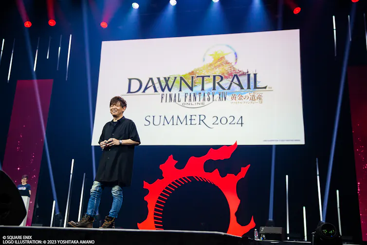 Yoshida on stage with Dawntrail announcement on the screen behind him.