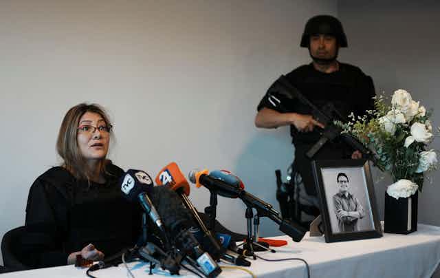 Veronica Sarauz, widow of presidential candidate Fernando Villavicencio, speaks to the press with a picture of her late husband and an armed security guard.