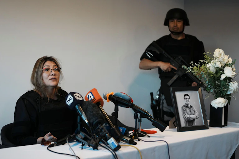 Veronica Sarauz, widow of presidential candidate Fernando Villavicencio, speaks to the press with a picture of her late husband and an armed security guard.