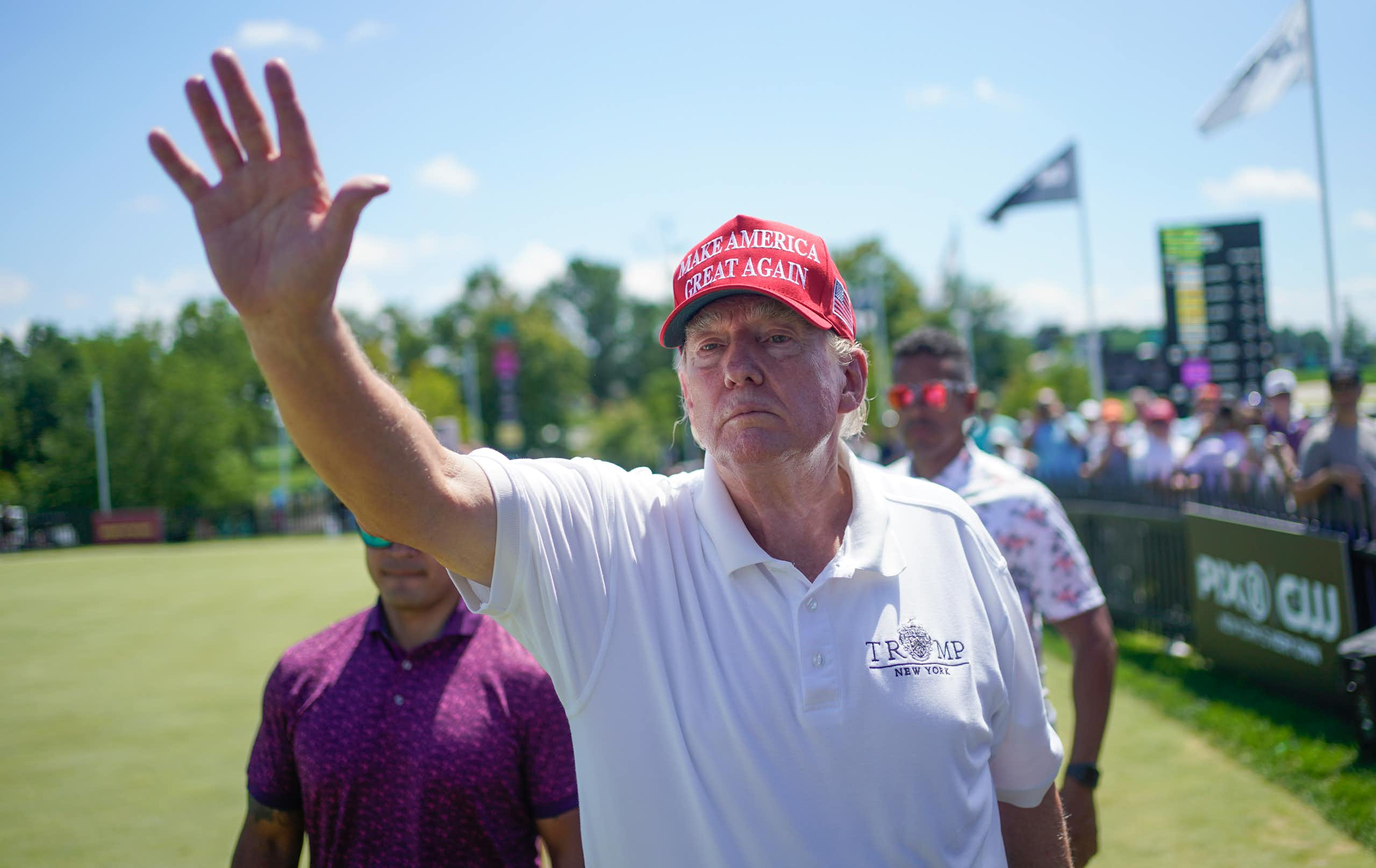 Un homme vêtu d'une chemise de golf blanche et portant une casquette rouge salue sans sourire.