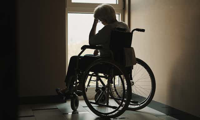 Silhouette of an older woman in a wheelchair, looking out of a window