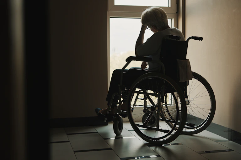 Silhouette of an older woman in a wheelchair, looking out of a window