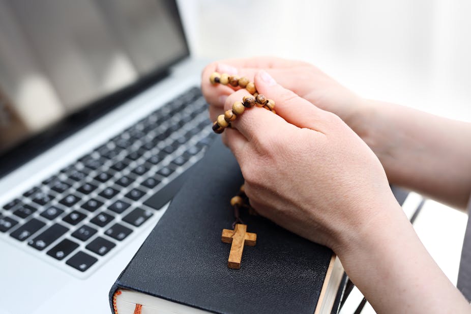 A woman prays on a rosary in front of a computer.