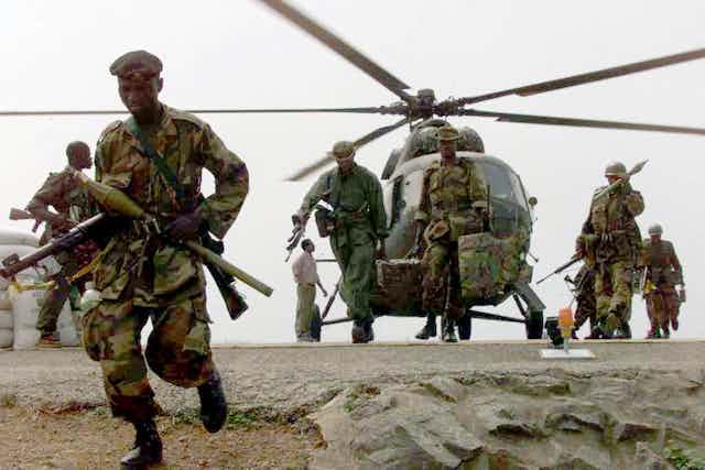 Armed men in military uniform disembarking from a helicopter