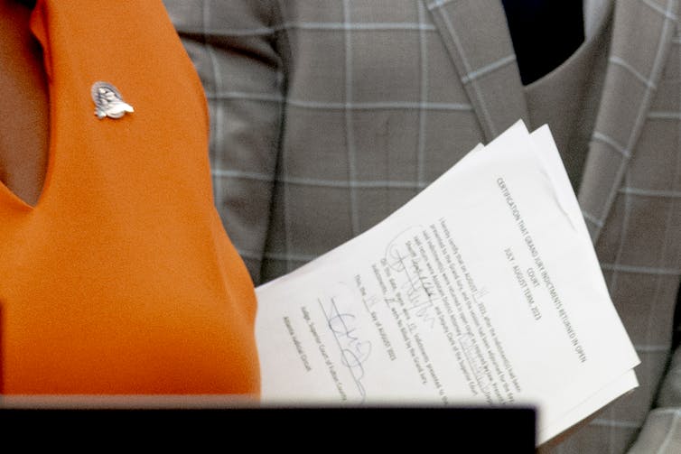 A close up of a legal document is seen against a woman's orange dress.