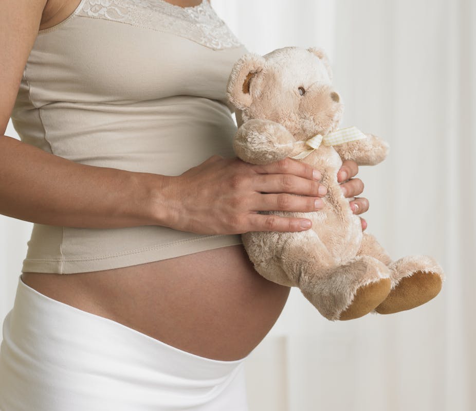 Person shown holding a teddy bear in front of a pregnant exposed belly.