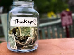 Tip jar full of dollar bills with a 'thank you' written on a strip of tape adhered to it