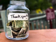 Tip jar full of dollar bills with a 'thank you' written on a strip of tape adhered to it