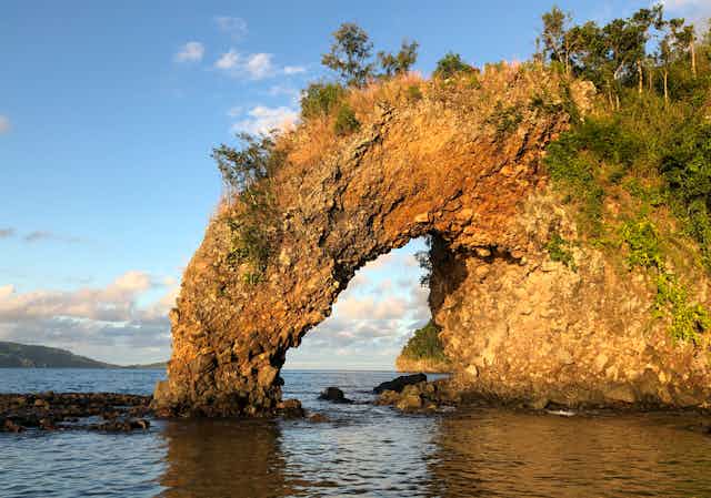 An orange rock jutting out of the sea with a large arch on one side