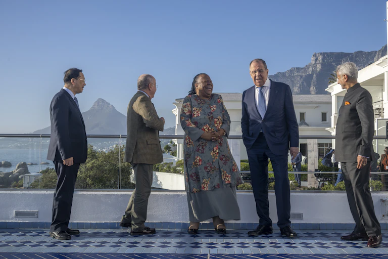 Four men and a woman stand and laugh in front of a white building and mountains.