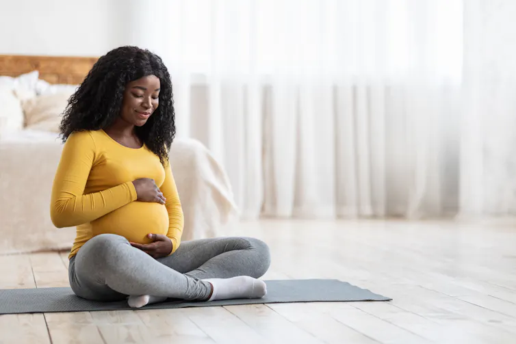 A pregnant woman wearing a yellow top clutches her belly.