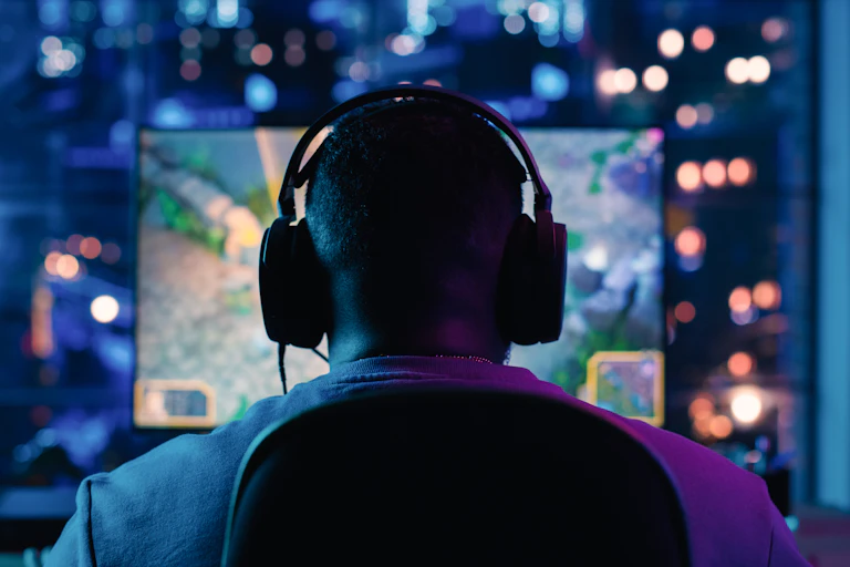 Photo of a man playing a video game with headphones in a darkened room.
