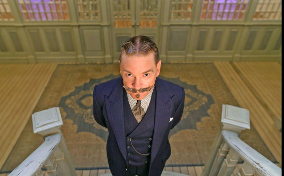 A man with a flamboyant moustache and wearing a three piece suit stares at the camera.