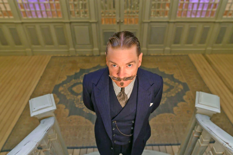 A man with a flamboyant moustache and wearing a three piece suit stares at the camera.