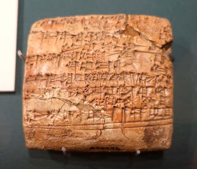 A brown-colored clay tablet with cracks and cuneiform on it.