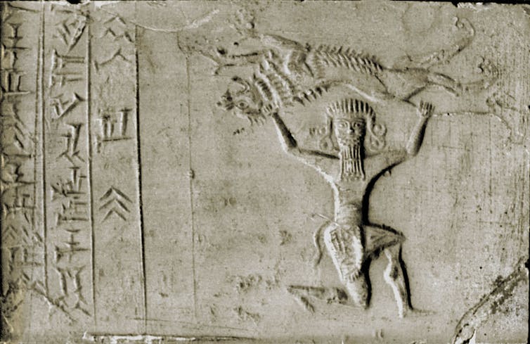 A slate-colored ancient seal has characters and an etching of a kneeling man holding a lion above his head.