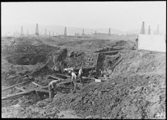 A black and white photograph shows a group of workers using equipment to dig out a pit.