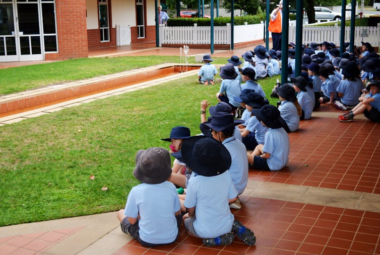 Children in uniform sit on the ground.