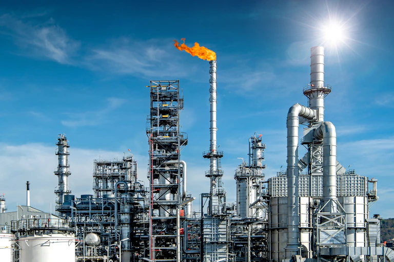 oil and gas refinery with flare of burning off and sun behind it