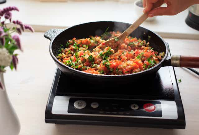 Induction cooking at home on a black portable cooker in cast iron cookware. Vegan meal with lentils, rice and vegetables
